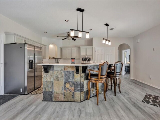 kitchen with arched walkways, light countertops, appliances with stainless steel finishes, light wood-type flooring, and a kitchen breakfast bar