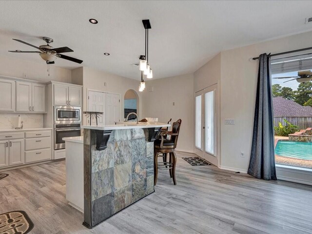 kitchen featuring a breakfast bar area, light wood-style floors, light countertops, appliances with stainless steel finishes, and a center island with sink