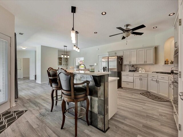 kitchen featuring a center island with sink, stainless steel fridge with ice dispenser, visible vents, light wood-style floors, and a kitchen bar