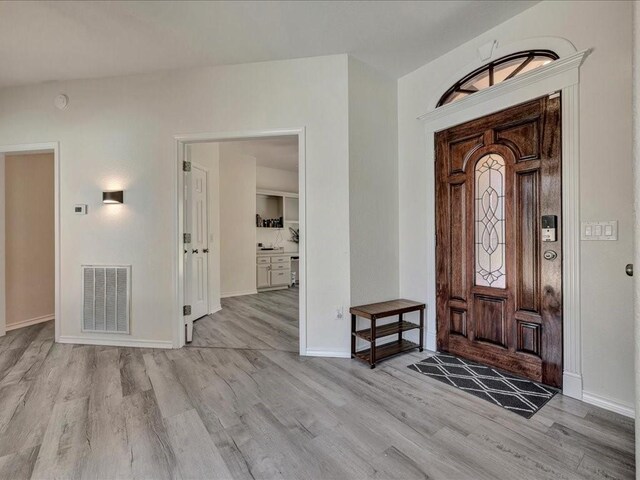 foyer entrance with baseboards, visible vents, and wood finished floors