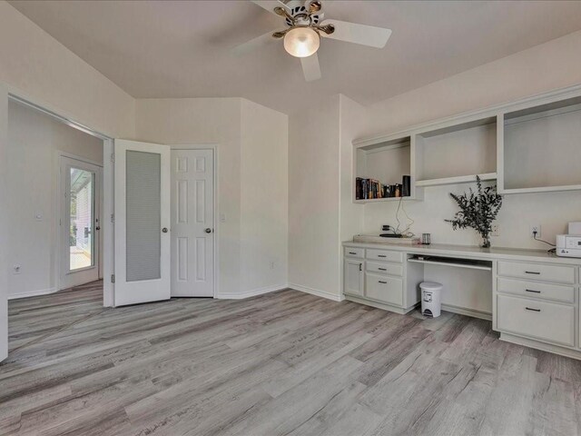 unfurnished office featuring light wood-type flooring, a ceiling fan, baseboards, and built in desk