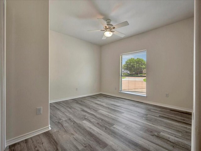 empty room with wood finished floors, a ceiling fan, and baseboards