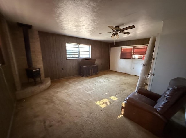 unfurnished room featuring a textured ceiling, a wood stove, ceiling fan, and wood walls