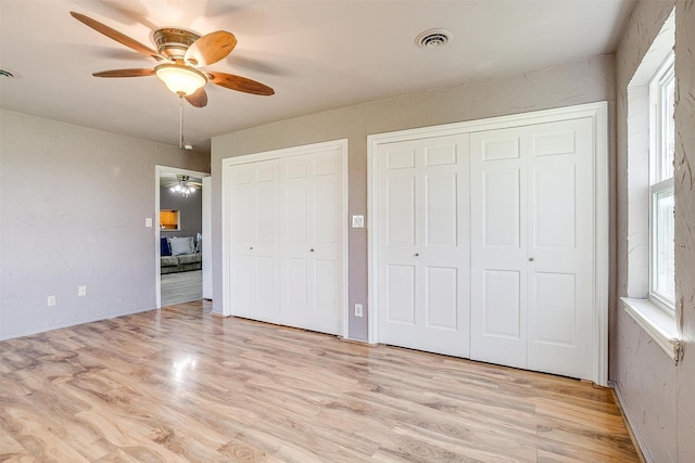 unfurnished bedroom with ceiling fan, light wood-type flooring, and two closets