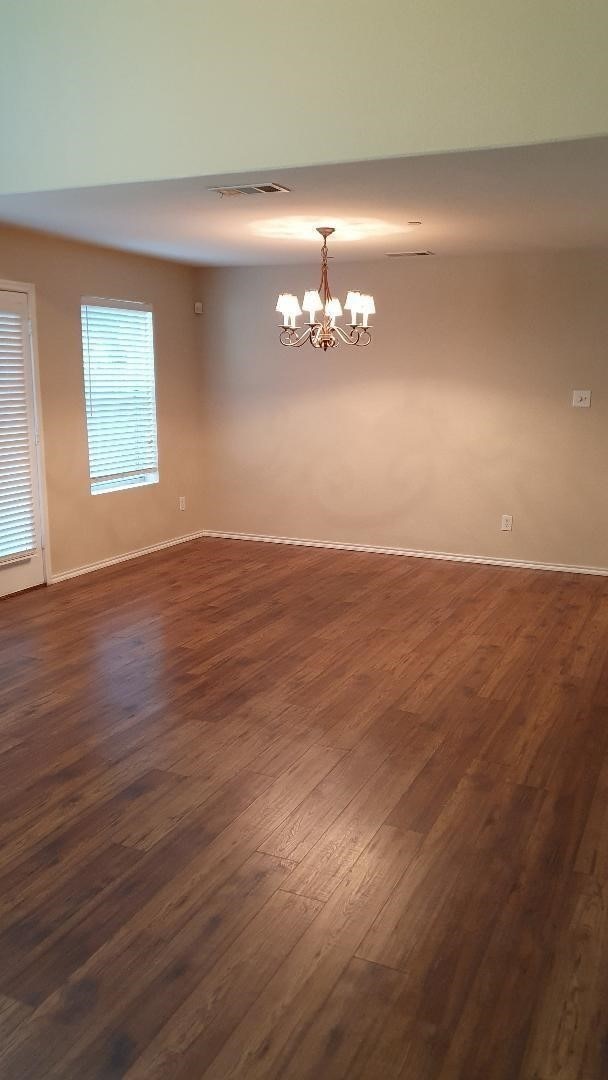 empty room featuring dark wood-type flooring and a notable chandelier