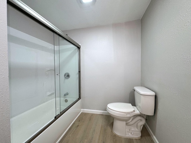 bathroom featuring enclosed tub / shower combo, toilet, and wood-type flooring