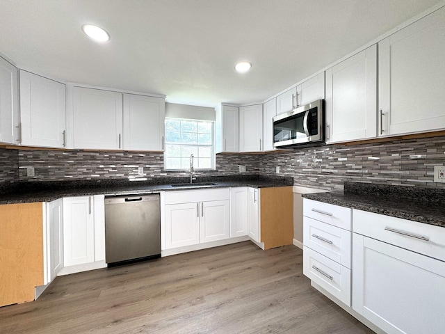 kitchen with appliances with stainless steel finishes, tasteful backsplash, sink, light hardwood / wood-style flooring, and white cabinetry