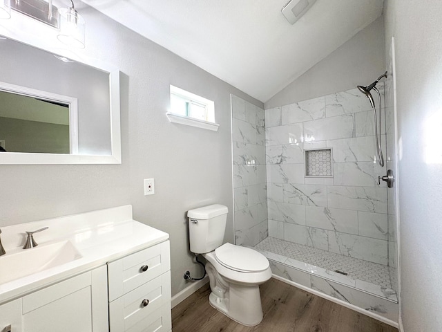 bathroom featuring a tile shower, wood-type flooring, vaulted ceiling, toilet, and vanity