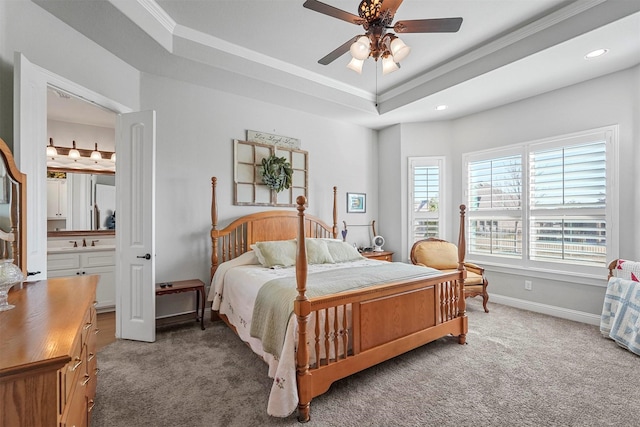 carpeted bedroom featuring a tray ceiling, ensuite bath, ceiling fan, and ornamental molding