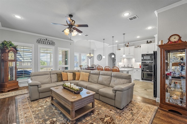 living room featuring hardwood / wood-style flooring, crown molding, and ceiling fan with notable chandelier