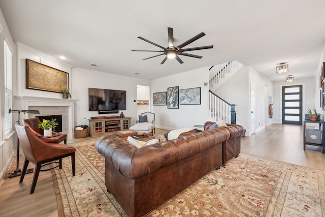 living room featuring ceiling fan, light hardwood / wood-style floors, and a tile fireplace