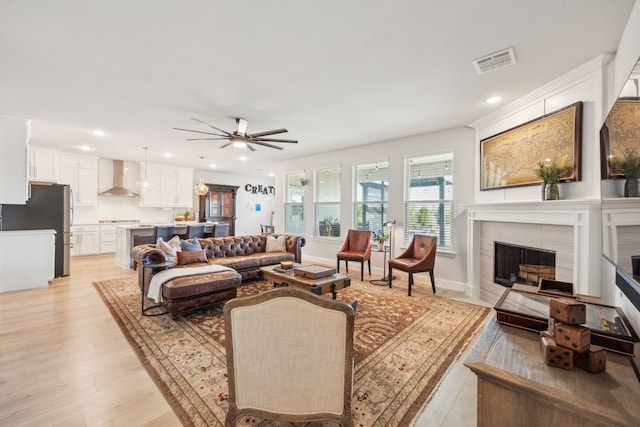 living room featuring ceiling fan, a tiled fireplace, and light wood-type flooring