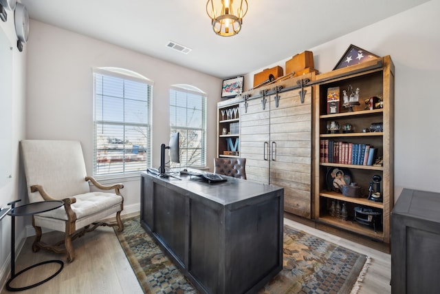 home office featuring hardwood / wood-style flooring, a barn door, and an inviting chandelier