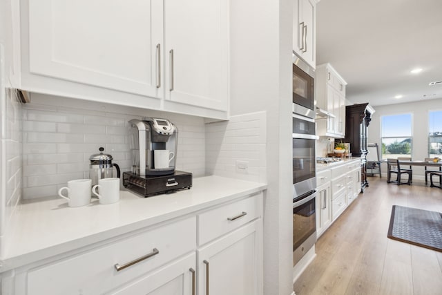 kitchen featuring white cabinetry, backsplash, light wood-type flooring, and appliances with stainless steel finishes