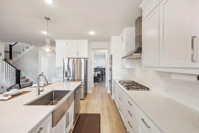 kitchen featuring white cabinetry, appliances with stainless steel finishes, wall chimney exhaust hood, and hanging light fixtures