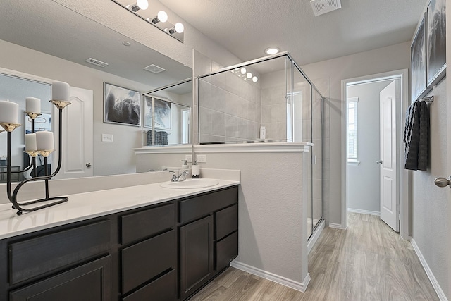 bathroom with a shower with door, vanity, hardwood / wood-style floors, and a textured ceiling