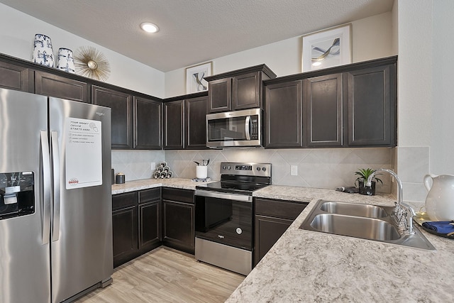 kitchen with tasteful backsplash, sink, stainless steel appliances, and light hardwood / wood-style floors