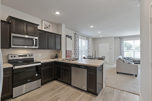 kitchen featuring kitchen peninsula, appliances with stainless steel finishes, sink, light hardwood / wood-style floors, and plenty of natural light