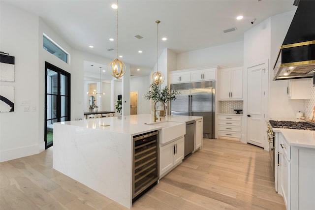 kitchen with tasteful backsplash, a center island with sink, white cabinetry, wine cooler, and hanging light fixtures