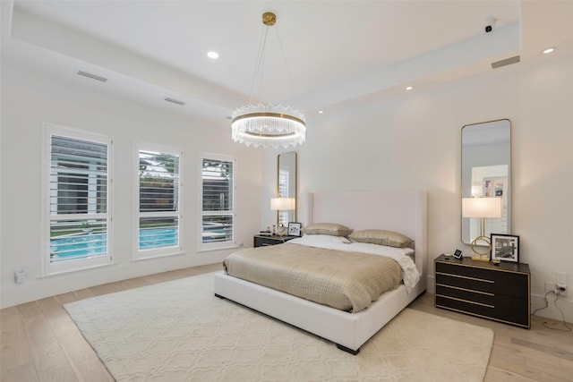 bedroom featuring a chandelier, light wood-type flooring, and a raised ceiling