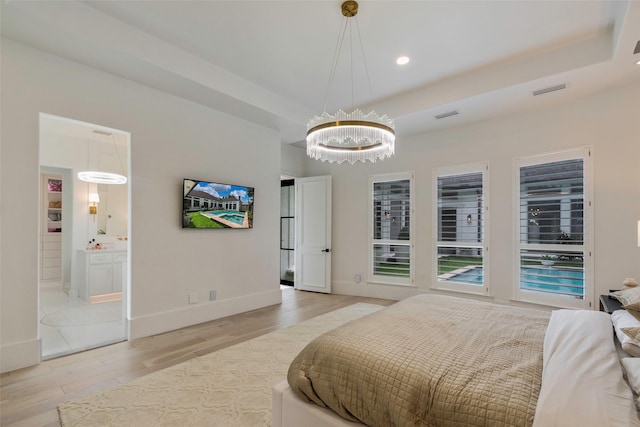 bedroom featuring ensuite bath, light hardwood / wood-style flooring, a notable chandelier, a tray ceiling, and access to outside