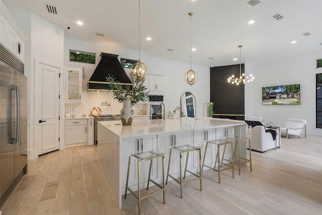 kitchen with white cabinetry, a large island, stainless steel appliances, backsplash, and custom exhaust hood