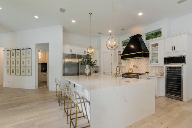 kitchen featuring custom range hood, white cabinetry, high quality appliances, wine cooler, and a large island