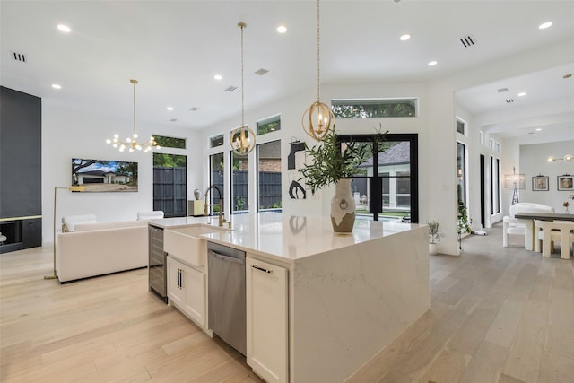 kitchen featuring dishwasher, decorative light fixtures, white cabinets, and an island with sink