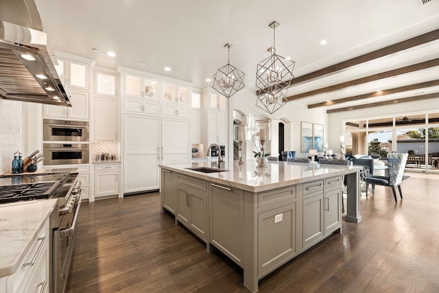 kitchen with island range hood, decorative light fixtures, sink, backsplash, and a kitchen island with sink