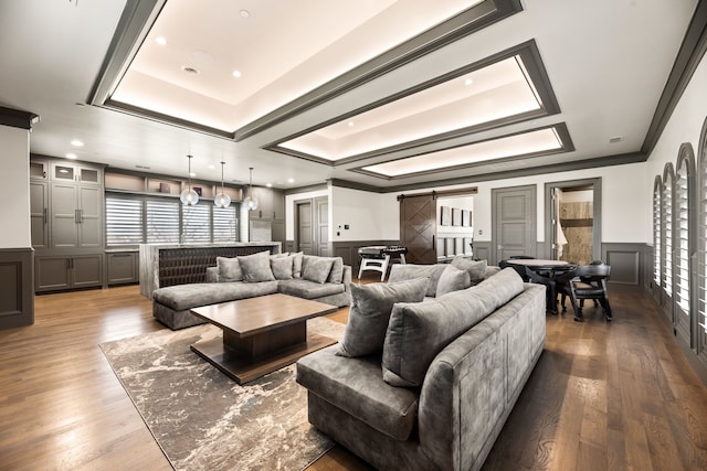 living room with wood-type flooring, a barn door, crown molding, and a tray ceiling