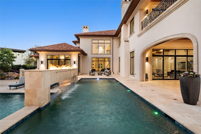 back house at dusk featuring a bar, a patio, pool water feature, and a balcony