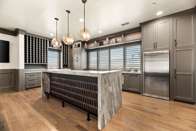 interior space with light stone counters, hanging light fixtures, gray cabinets, and built in fridge