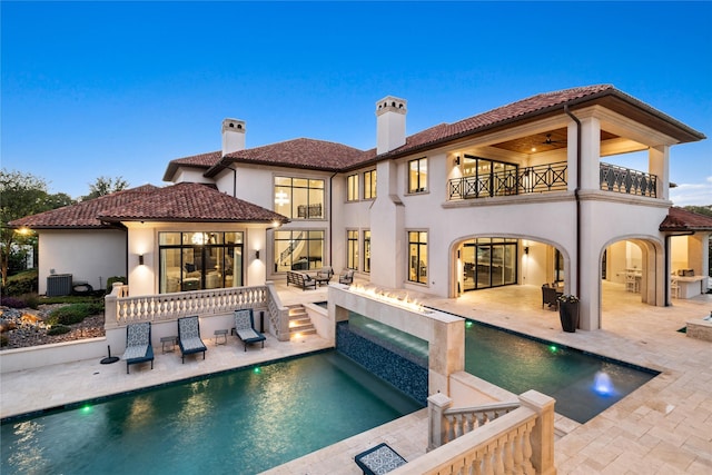 back house at dusk with a balcony, cooling unit, ceiling fan, a fire pit, and a patio