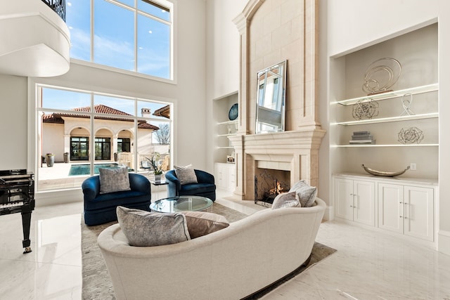 living room with built in shelves, a fireplace, and a towering ceiling