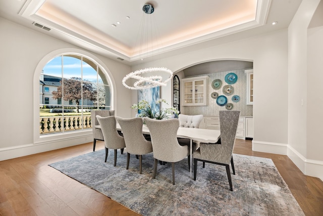 dining space featuring an inviting chandelier, hardwood / wood-style floors, and a raised ceiling