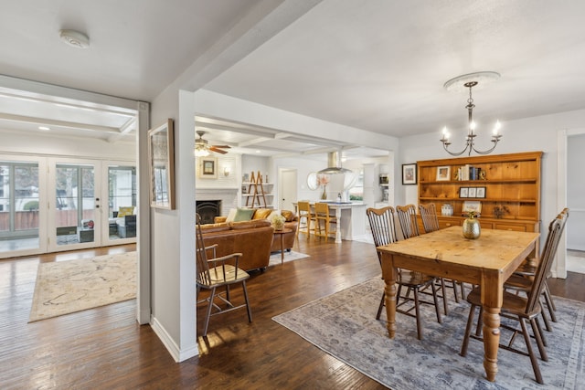 dining room with ceiling fan with notable chandelier, beam ceiling, dark hardwood / wood-style flooring, and a fireplace