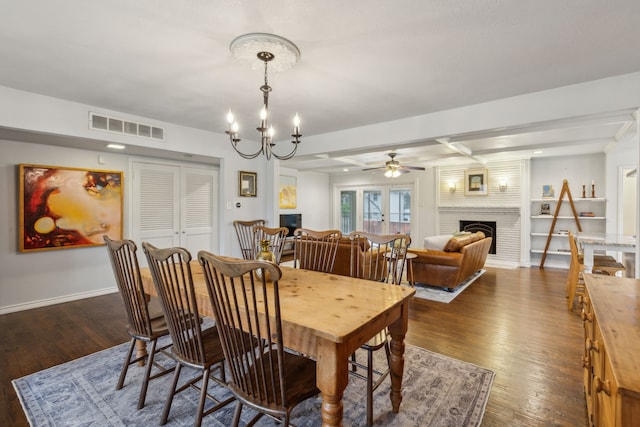 dining space with beam ceiling, a large fireplace, ceiling fan with notable chandelier, and dark hardwood / wood-style floors