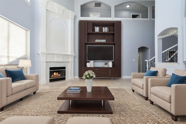 living room with arched walkways, visible vents, stairway, a high ceiling, and a high end fireplace