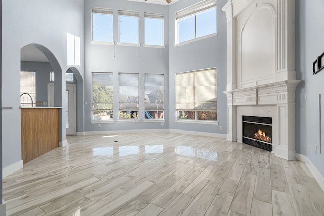 unfurnished living room with light wood-type flooring, a fireplace, arched walkways, and baseboards