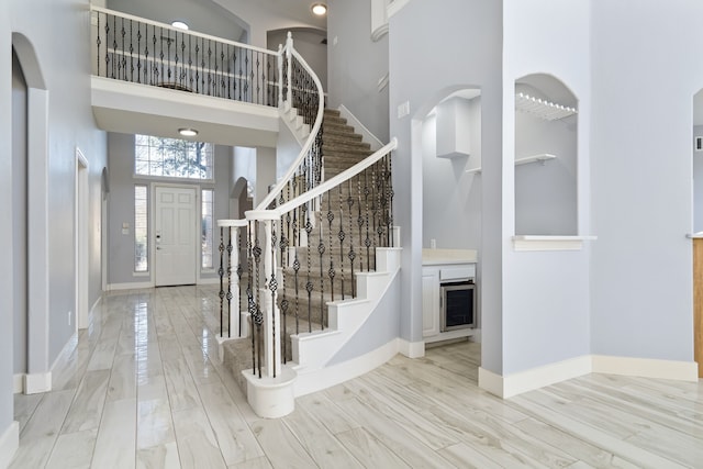 entryway with baseboards, arched walkways, a towering ceiling, stairway, and wood finished floors