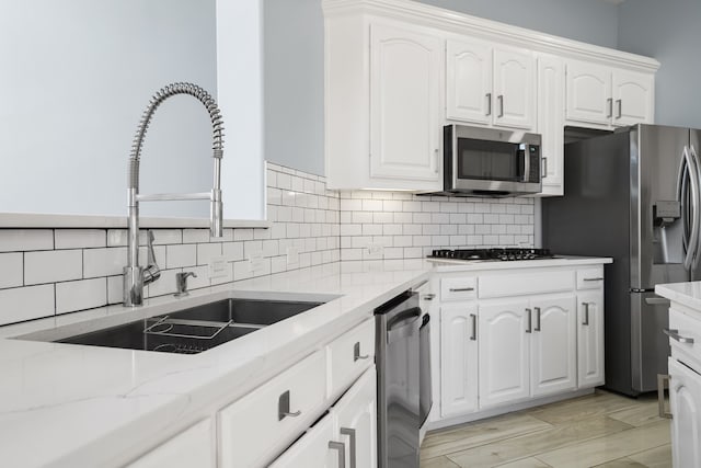 kitchen featuring light stone counters, stainless steel appliances, a sink, white cabinetry, and backsplash