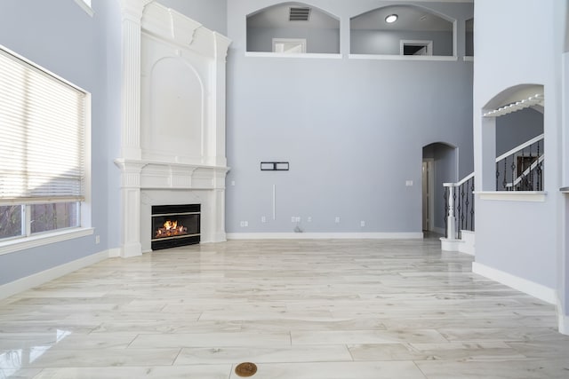 unfurnished living room with arched walkways, stairway, a towering ceiling, a premium fireplace, and wood finished floors