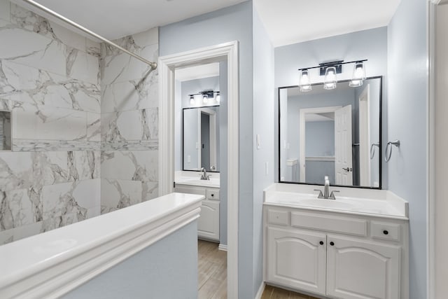 bathroom featuring a shower, two vanities, a sink, and wood finished floors