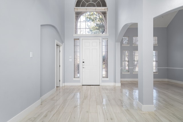 foyer featuring a high ceiling, baseboards, arched walkways, and wood finished floors