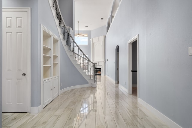 entrance foyer with arched walkways, a towering ceiling, stairway, light wood-style floors, and baseboards