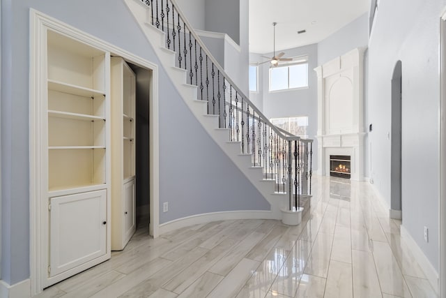 entryway with a ceiling fan, stairway, wood tiled floor, a high ceiling, and a high end fireplace