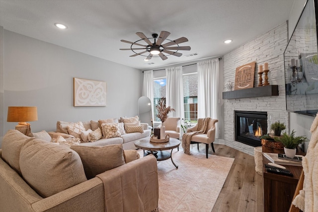 living room with ceiling fan, wood-type flooring, and a stone fireplace