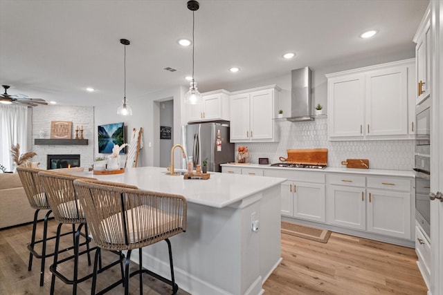 kitchen with appliances with stainless steel finishes, an island with sink, white cabinetry, and wall chimney range hood