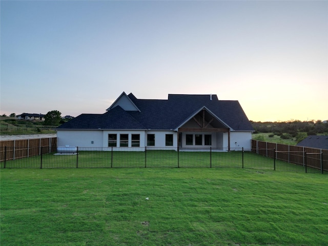 back house at dusk featuring a lawn