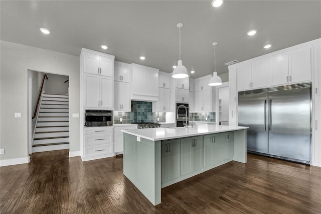 kitchen featuring pendant lighting, white cabinetry, an island with sink, and built in refrigerator